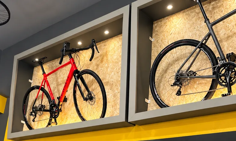 Bicicletas com guidão drop, vermelha e grafite, expostas em nichos iluminados acima da parede amarela